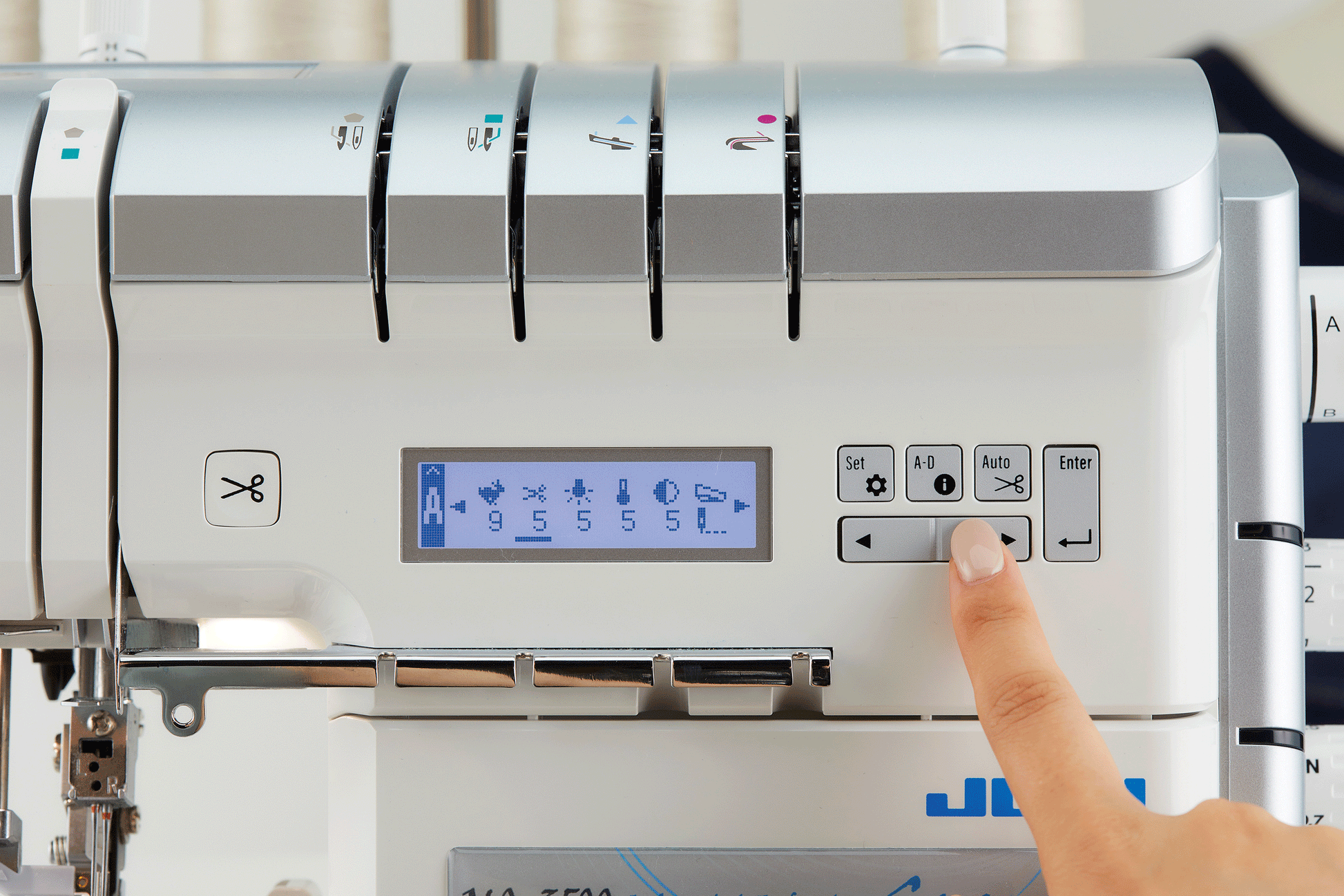 The LCD screen of the JUKI Akane MO-3000QVP showing a stitch diagram and its settings, with a finger on the arrow keys and the color marked thread guides above.