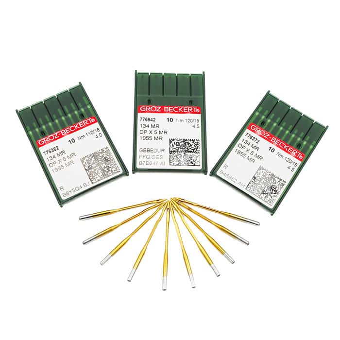 Three green plastic cases of Groz-Beckert sewing machine needles with labels facing forward, and nine gold sewing machine needles arranged in a fan shape in front of the cases, on a white background.