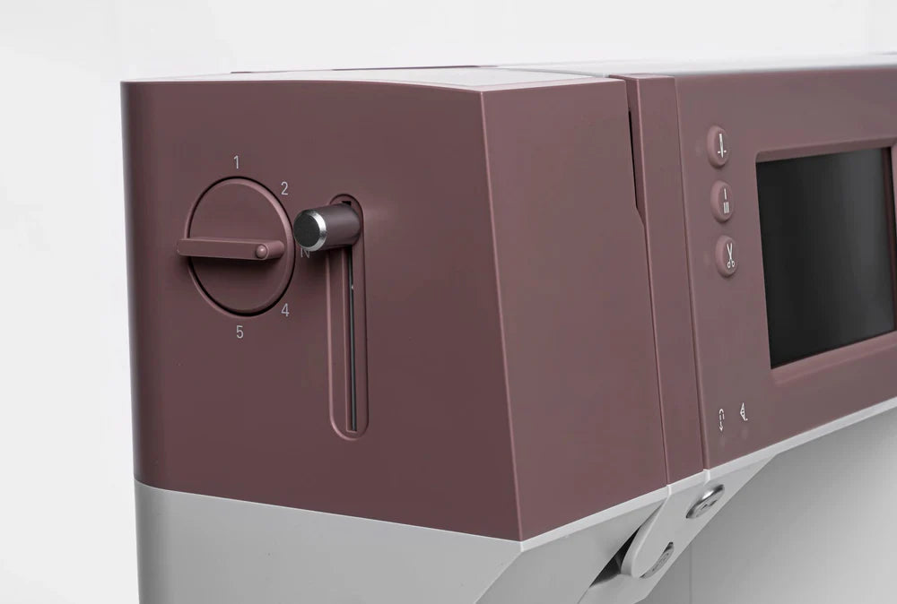 Close-up of a Quilted Joy Pfaff Quilt Ambition 635 Sewing and Quilting Machine in maroon and light gray, showing its numbered dial at 2, screen, buttons, flat control panel, and Integrated Dual Feed Technology.