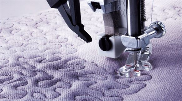 Close-up of the SVP Pfaff Passport 2.0 sewing machine needle and foot in sharp focus as they stitch a detailed free-motion quilted pattern on light fabric.