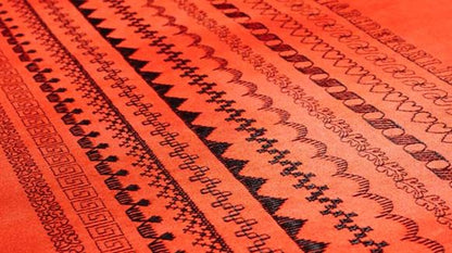 Close-up of red fabric with horizontal rows of black geometric and decorative patterns, such as zigzags and hearts—beautifully stitched with the precision of the SVP Pfaff Passport 2.0 compact sewing machine.