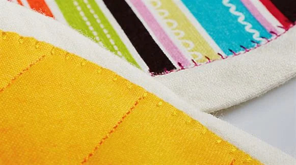 Close-up of yellow and multicolored fabrics joined with neat white stitches, created using the SVP Pfaff Passport 2.0 compact sewing machine.