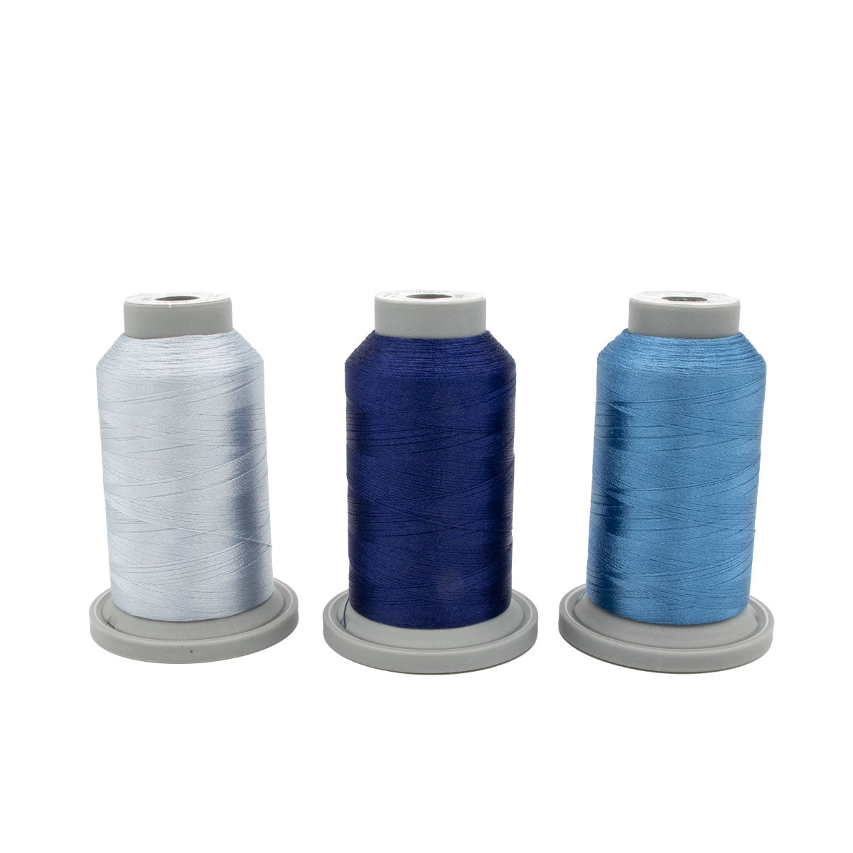 Three large spools of Hab+Dash Polar Prism Glide Thread of the Month Bundle, in white, dark blue, and light blue with gray bases, are arranged side by side against a white background—the perfect set for your quilting projects.