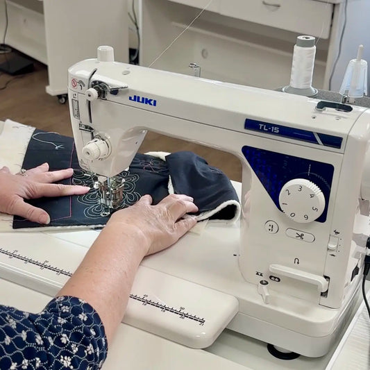 Someone uses a Juki Mechanical Pixie Playdate to stitch floral fabric in a bright room, wearing a blue patterned sleeve—ideal for anyone attending a quilting sewing class.