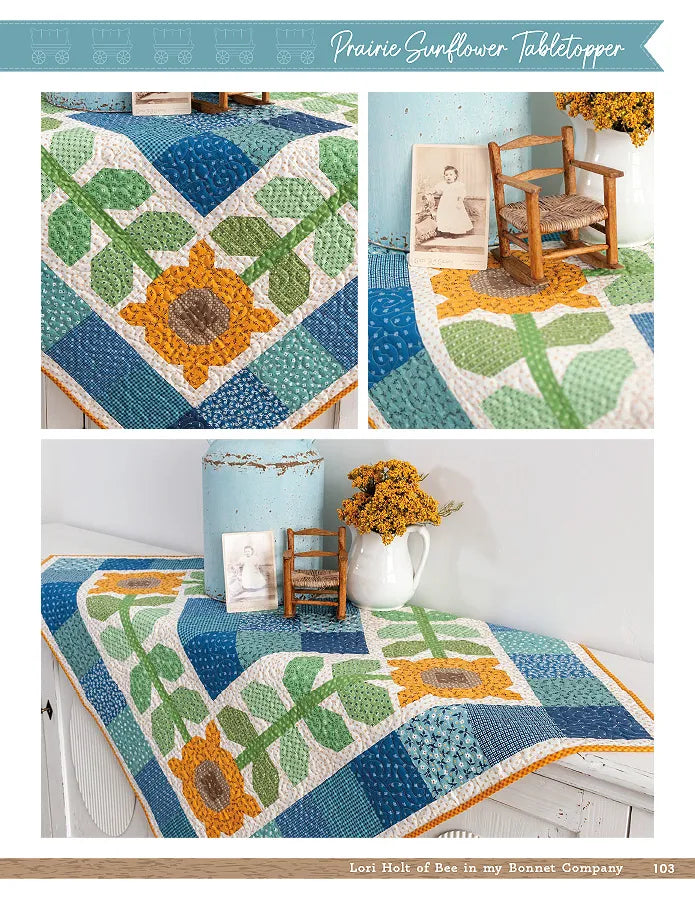 A table topper made with Lori Holt patterns from the Checker Distributor Prairie Home Quilt Book, featuring sunflower and leaf designs in blue, green, yellow, and white—shown on a table with blue canister and yellow flowers.