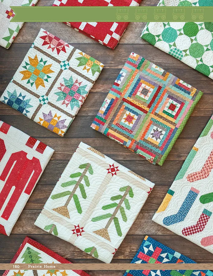 A top-down view of colorful, folded quilts with tree, star, patchwork square, stocking, and red pajama patterns—signature styles from Lori Holt's Prairie Home Quilt Book by Checker Distributor—arranged on a wooden surface.