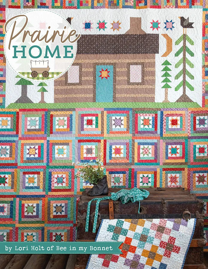 A vibrant patchwork star and square quilt hangs below a log cabin scene with trees, bird, and stars—quilt patterns inspired by the Prairie Home Quilt Book from Checker Distributor—adding charm to any space.