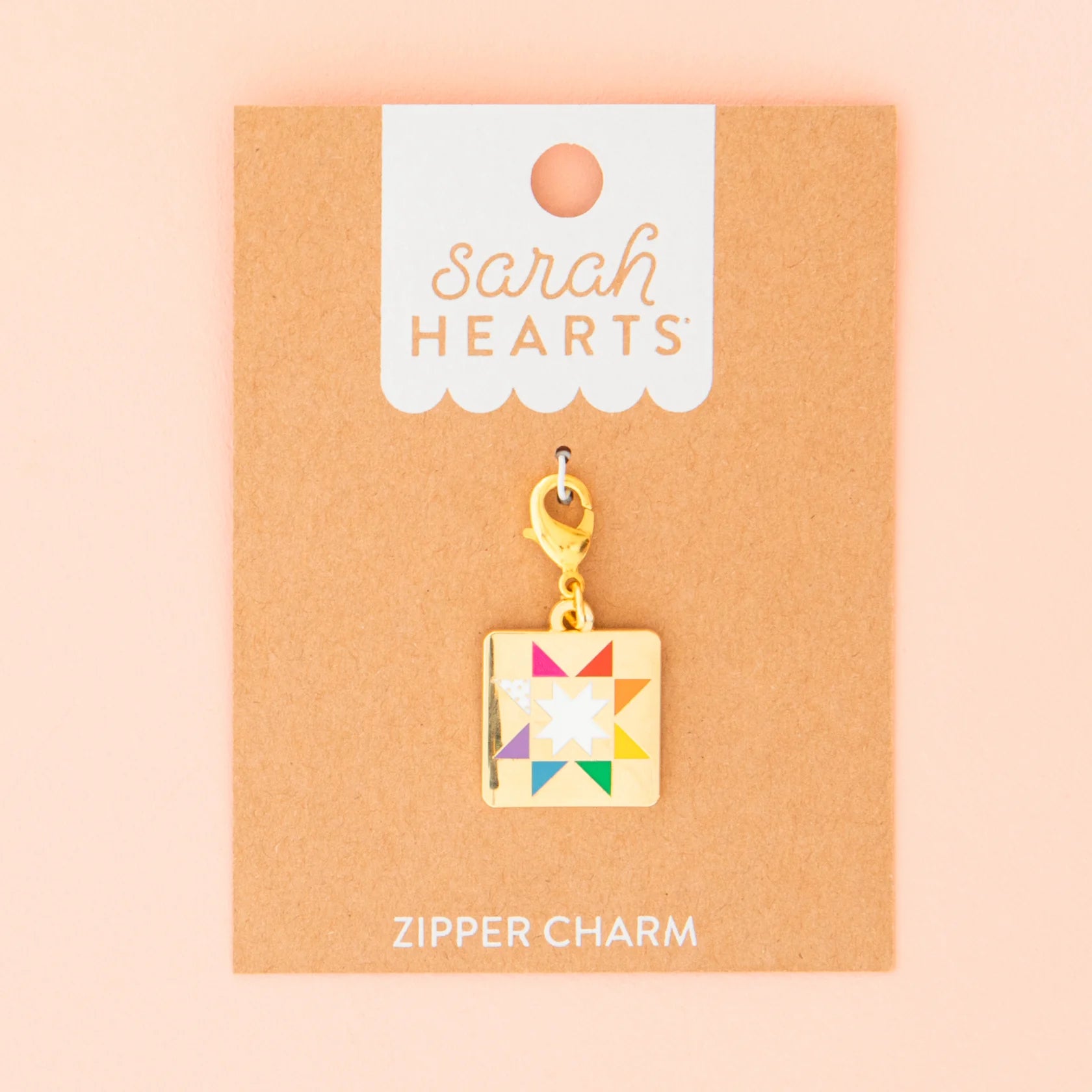 The Quilt Star Zipper Charm by Sarah Hearts features a colorful quilt star design and comes attached to a brown card labeled "Sarah Hearts" and "Zipper Charm" on a peach background.