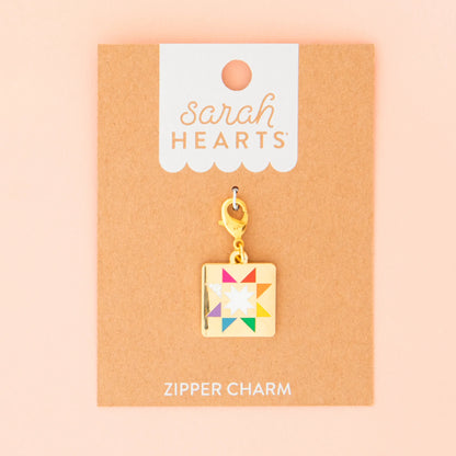 The Quilt Star Zipper Charm by Sarah Hearts features a colorful quilt star design and comes attached to a brown card labeled "Sarah Hearts" and "Zipper Charm" on a peach background.