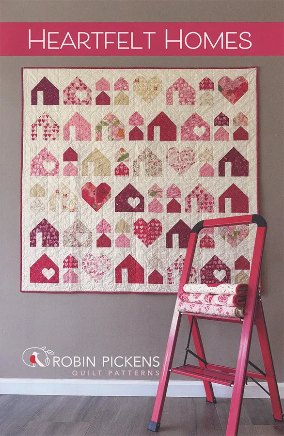 A quilt with red, pink, and cream house and heart designs hangs above a red step ladder holding three rolls of fabric. "Heartfelt Homes Quilt Pattern" by United Notions is displayed on the image.