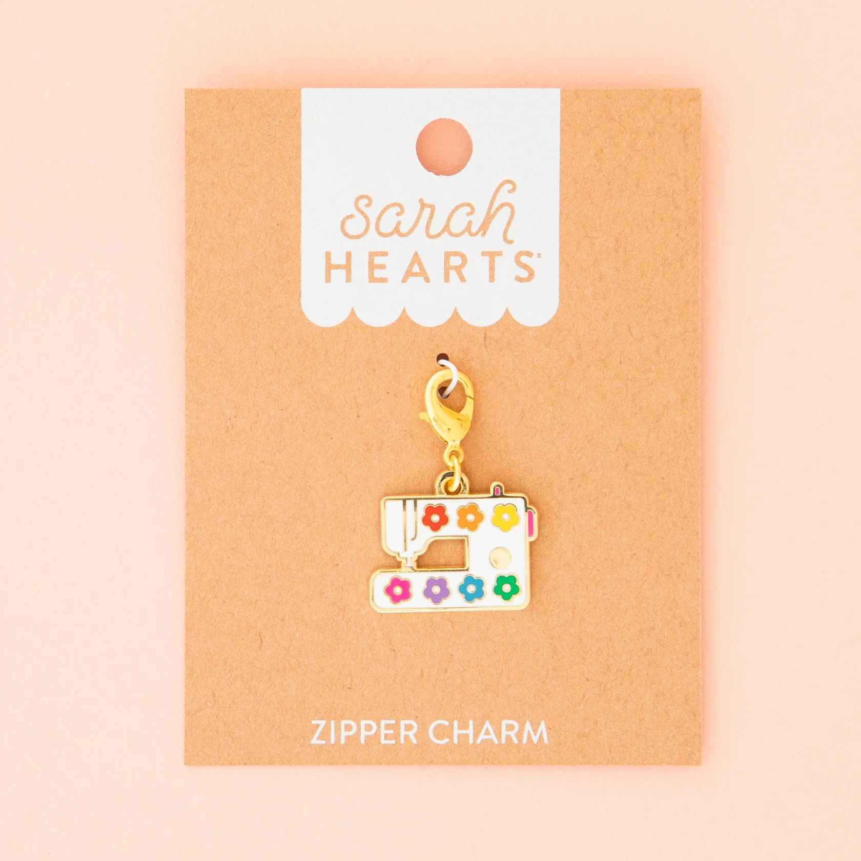 The Sarah Hearts Sewing Machine Zipper Charm features colorful flower details and a gold clasp, displayed on a brown card, making it the perfect accessory for any sewing enthusiast.