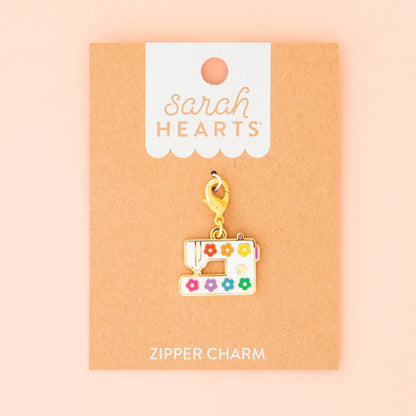 The Sarah Hearts Sewing Machine Zipper Charm features colorful flower details and a gold clasp, displayed on a brown card, making it the perfect accessory for any sewing enthusiast.