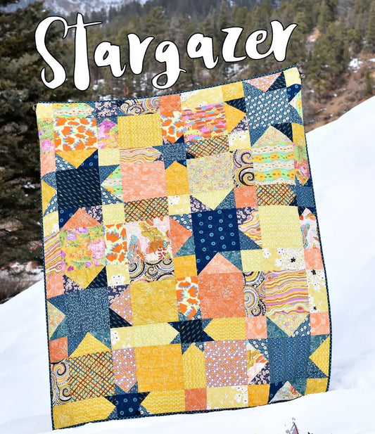 The Stargazer Quilt Class features a vibrant patchwork quilt with yellow, orange, and blue star blocks, displayed outdoors on snowy ground with trees and hills behind. "Stargazer Quilt Class" is written in bold white script at the top.