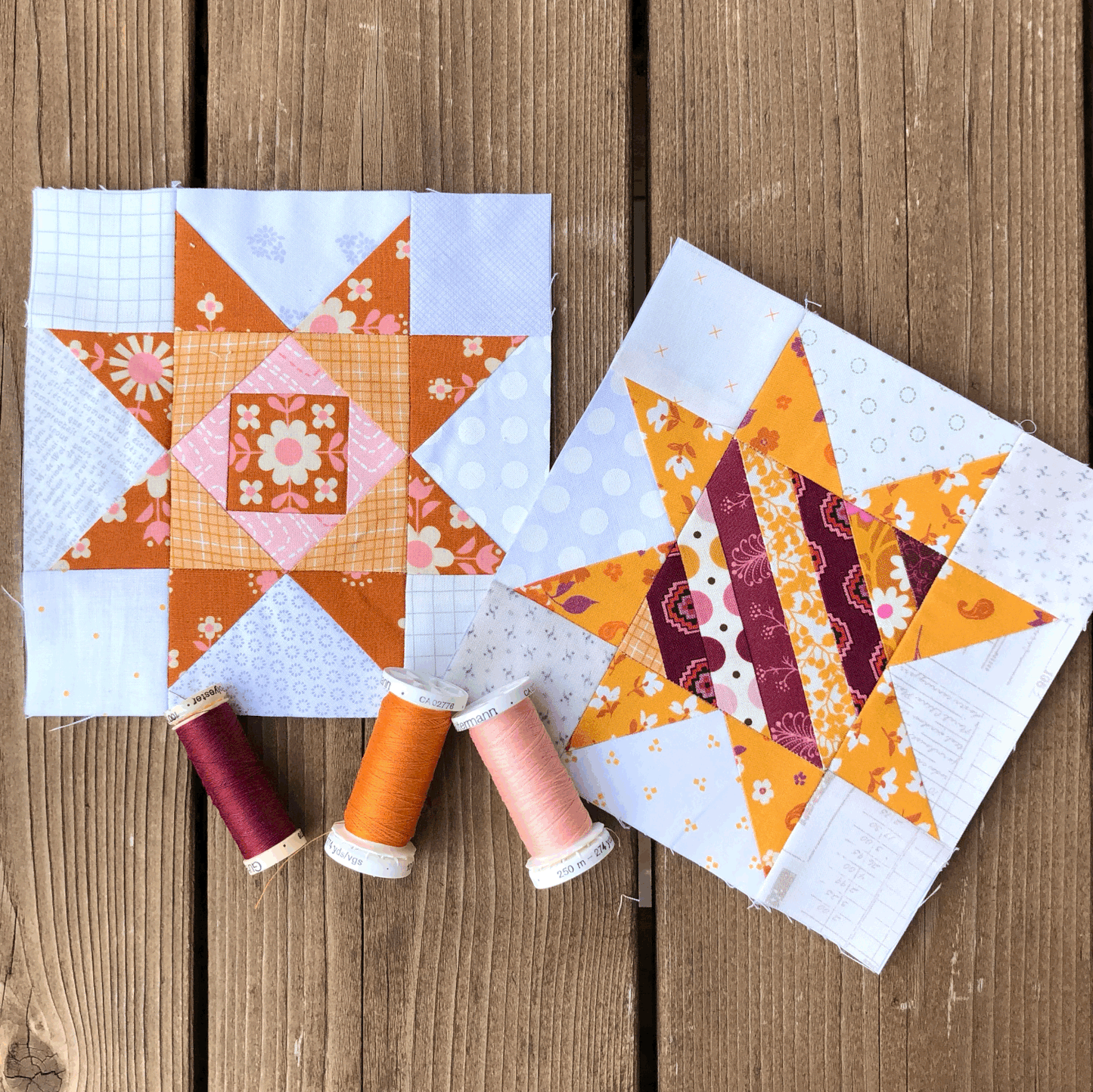 Quilted Joy's Scrappy Stars quilt blocks showcase vibrant orange, yellow, and purple fabrics on a wooden surface, with four matching thread spools in front. Made using paper piecing for precise star patterns.