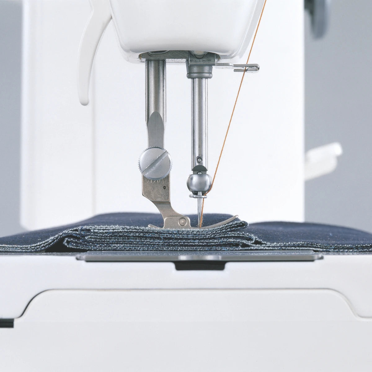 The JUKI TL-15 stitching through a folded stack of denim layers, the presser foot riding level over the bulk.