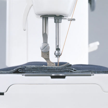 The JUKI TL-15 stitching through a folded stack of denim layers, the presser foot riding level over the bulk.