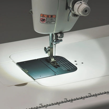 The needle area of the JUKI TL-15 lit by its LED against a dark background, with the inch markings along the front edge of the bed catching the light.
