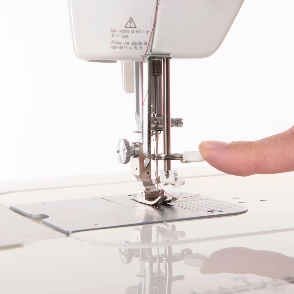 A finger pressing the automatic needle threader lever on the JUKI TL-15, with the needle and presser foot below.