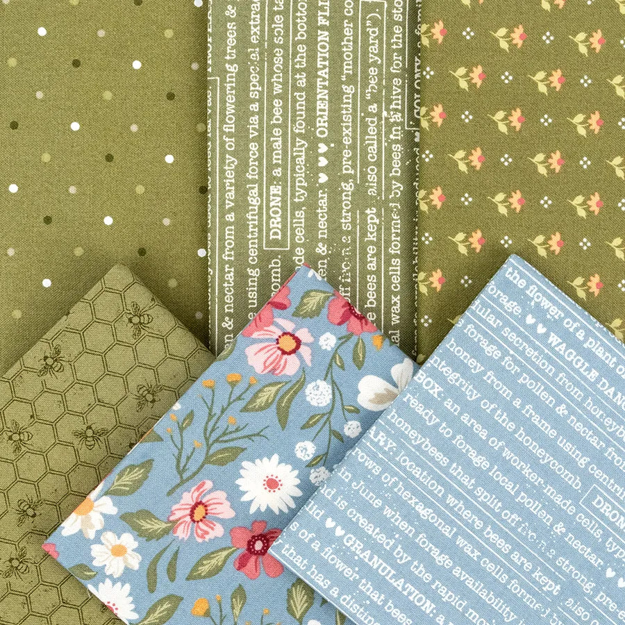 Five quilting cotton pieces are fanned out: three green prints with dots, flowers, or honeycomb from United Notions’ Wild Honey Charm Pack, plus two blue Moda fabrics with florals or white text.
