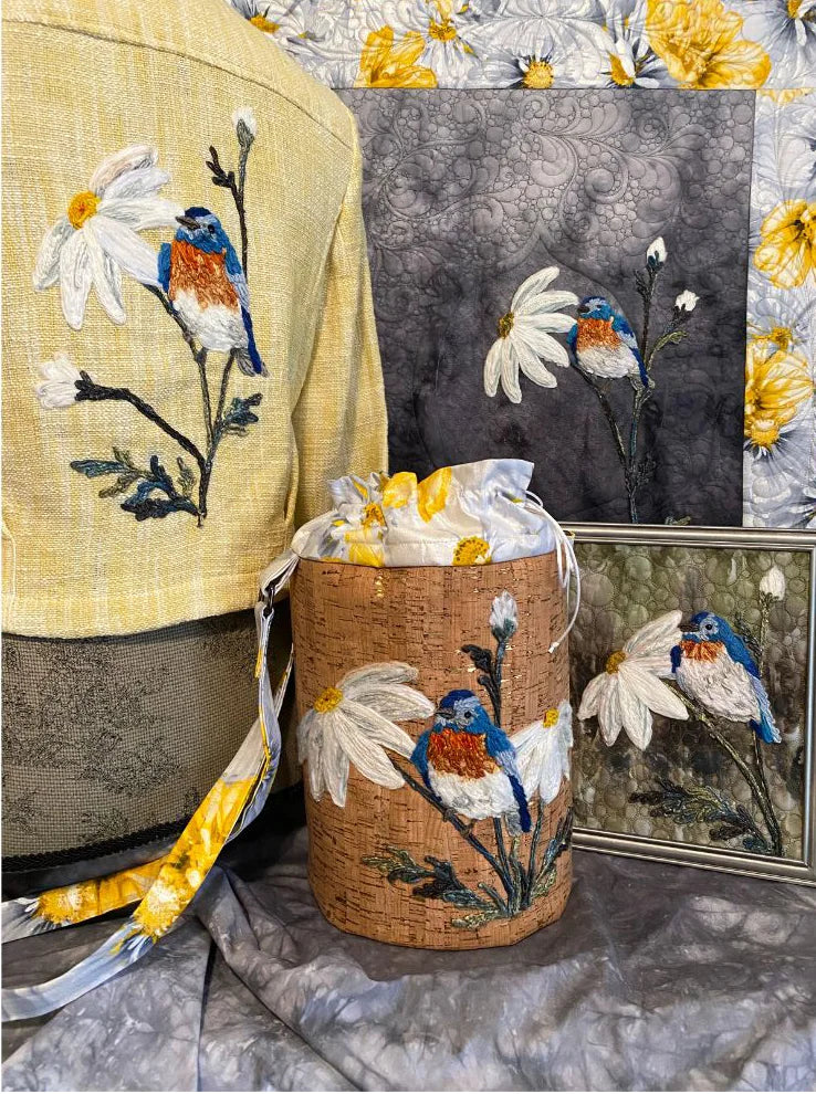 Discover embroidered items inspired by Bethanne Nemesh at the Yarn Couching Trunk Show on Friday, March 13th, 2026—featuring bluebirds, daisies, a yellow garment, quilted florals, a fabric bucket, and a framed piece for any quilting fan.
