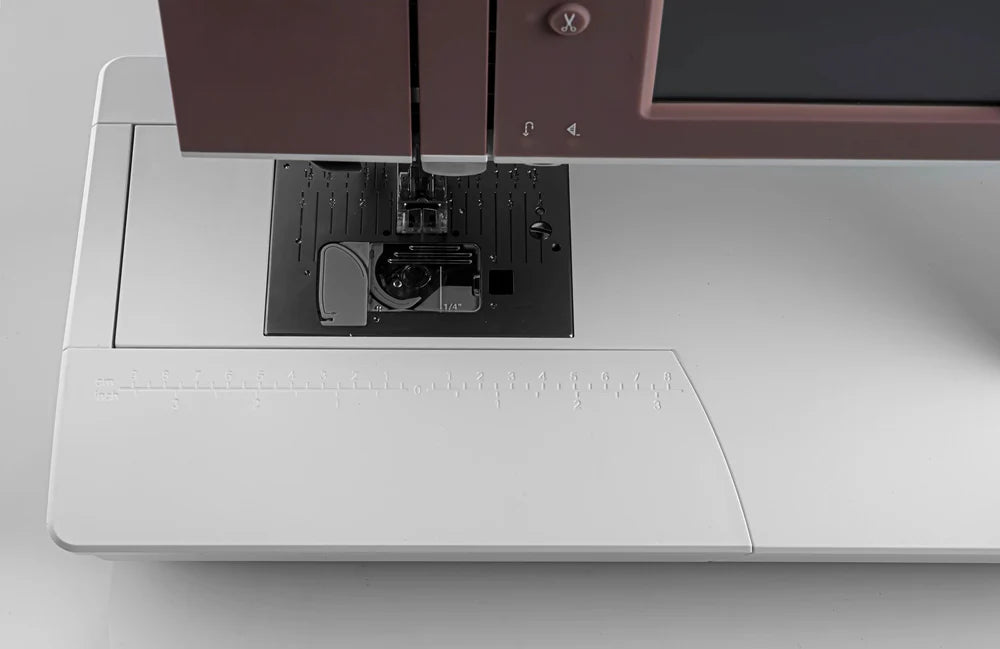 Close-up of the Pfaff Quilt Ambition 635 Sewing and Quilting Machine by Quilted Joy, highlighting the needle area with presser foot, needle plate guide markings, and touchscreen panel—ideal for quilting projects. Features a sleek white and silver design.