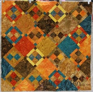 This batik wall hanging has an alternating four patch block on point. Longarm quilter Angela Huffman added the Brittany pantograph for an all over quilting design