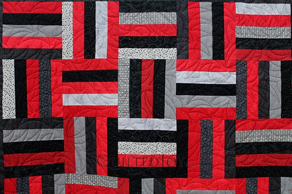 Karen made this Rail Fence quilt for her son and she has lots of hidden meanings in it's design. It's red, black, and grey, because he's an avid UofL supporter and it's quilted with footballs because he played while growing up.