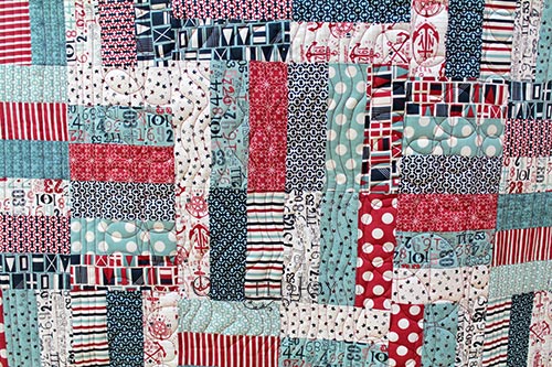 Close up of free motion quilting on split rail fence quilt with red, white, and blue nautical themed fabric.