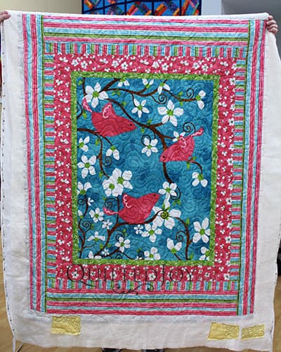 Kathy shows off her birds panel quilt after a longarm machine rental at Quilted Joy