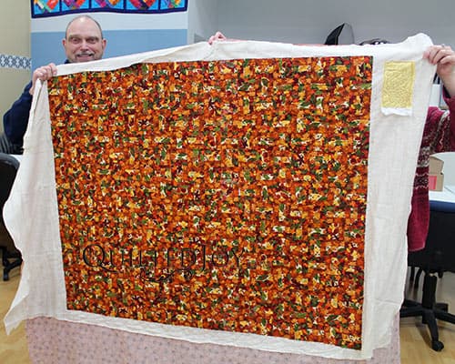 Dennis shows off his autumnal split rail fence quilt after longarm quilting at Quilted Joy