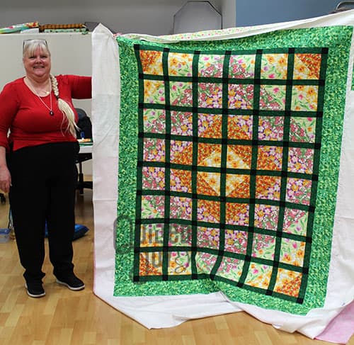 Betty shows off her latticework quilt after quilting it on a longarm machine at Quilted Joy