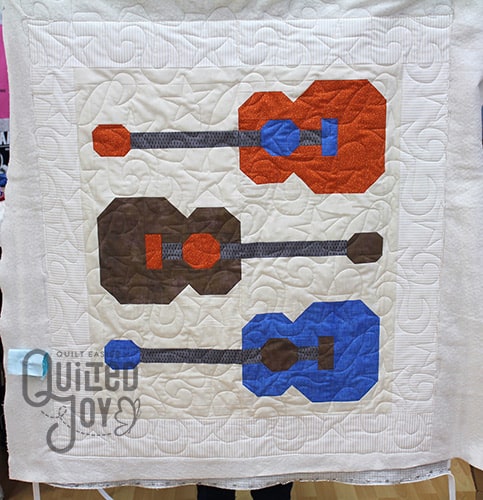 Colleen shows off her guitars quilt after quilting it on a longarm at Quilted Joy