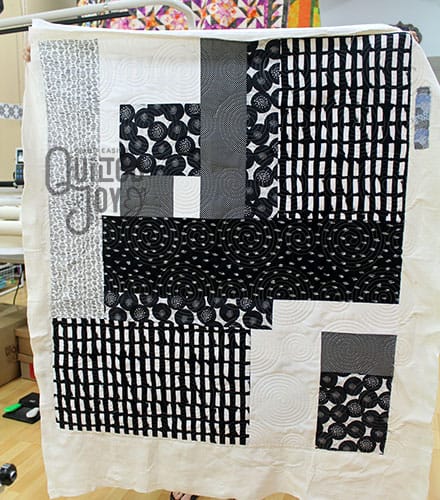 Darcy shows off her black and white quilt after renting a longarm machine at Quilted Joy