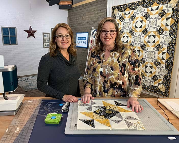 image of Angela Huffman and Sara Gallegos on Love of Quilting film set with a yellow and gold quilt called All the Buzz hanging in the background