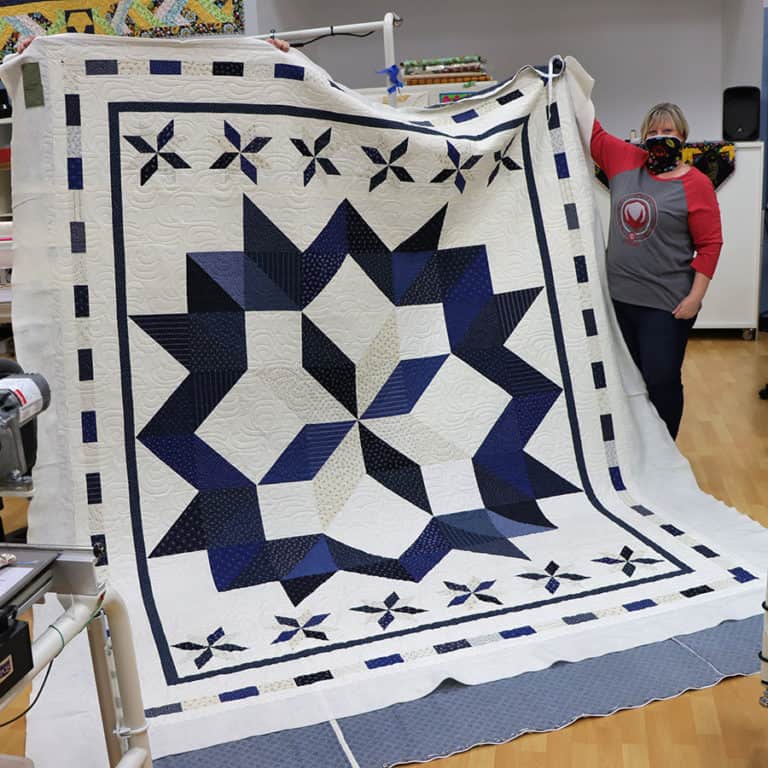 image of Kim showing off her Carpenter Star Quilt after quilting it at Quilted Joy on a APQS longarm quilting machine