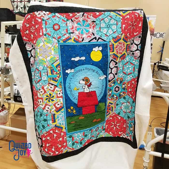 image of a quilt with a center illustration of Snoopy for the Peanuts comics on his red dog house surrounded by lots of color